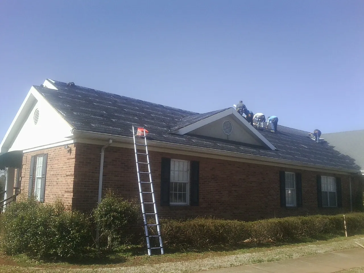 Crew tearing shingles off a brick ranch roof with a ladder set — Emergency Roof Repair work by our crew in Dighton