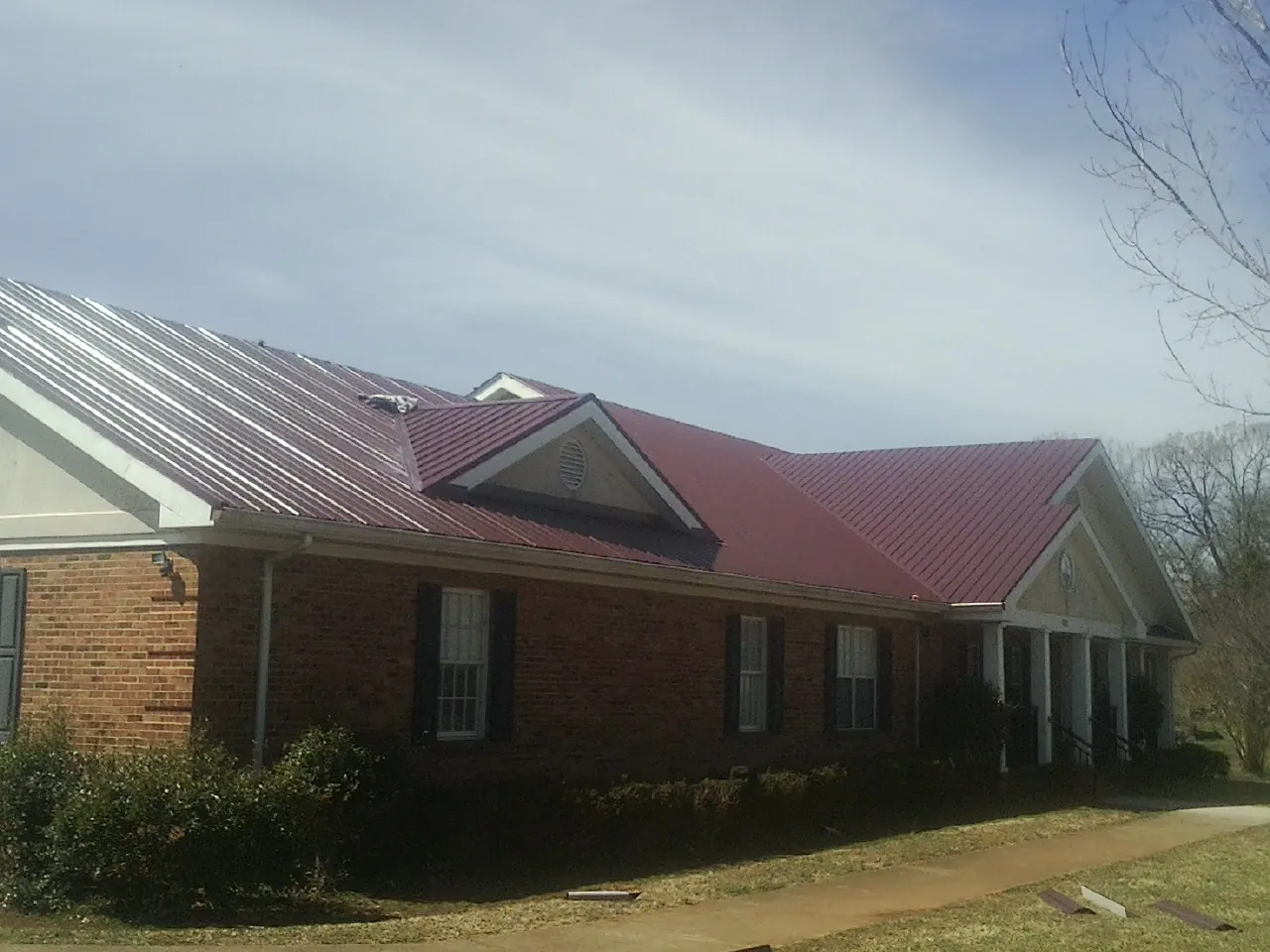 Red metal roof with gabled entries on a long brick building, from a Hail Damage Roof Repair job in Dighton