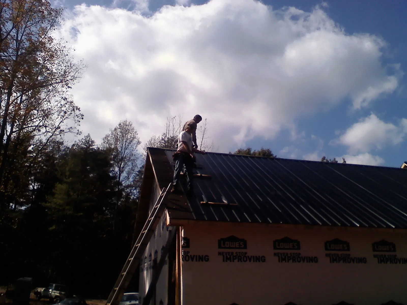 Roofer fastening dark metal panels high against a cloudy sky, from a Roof Inspection job in Dighton