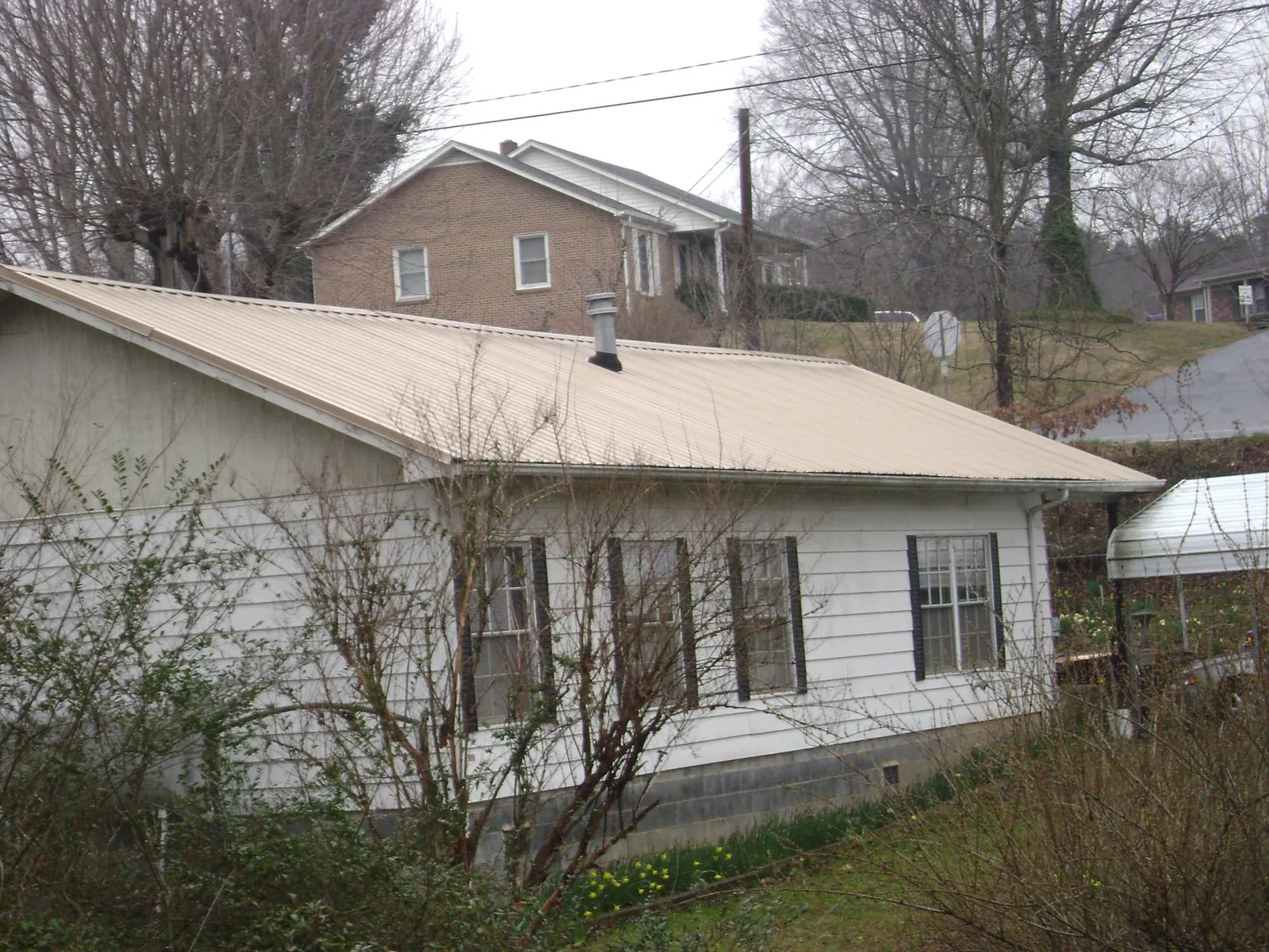 Tan metal roof on a white sided house set into a hillside — Commercial Roofing by Roofing Brothers in Dighton