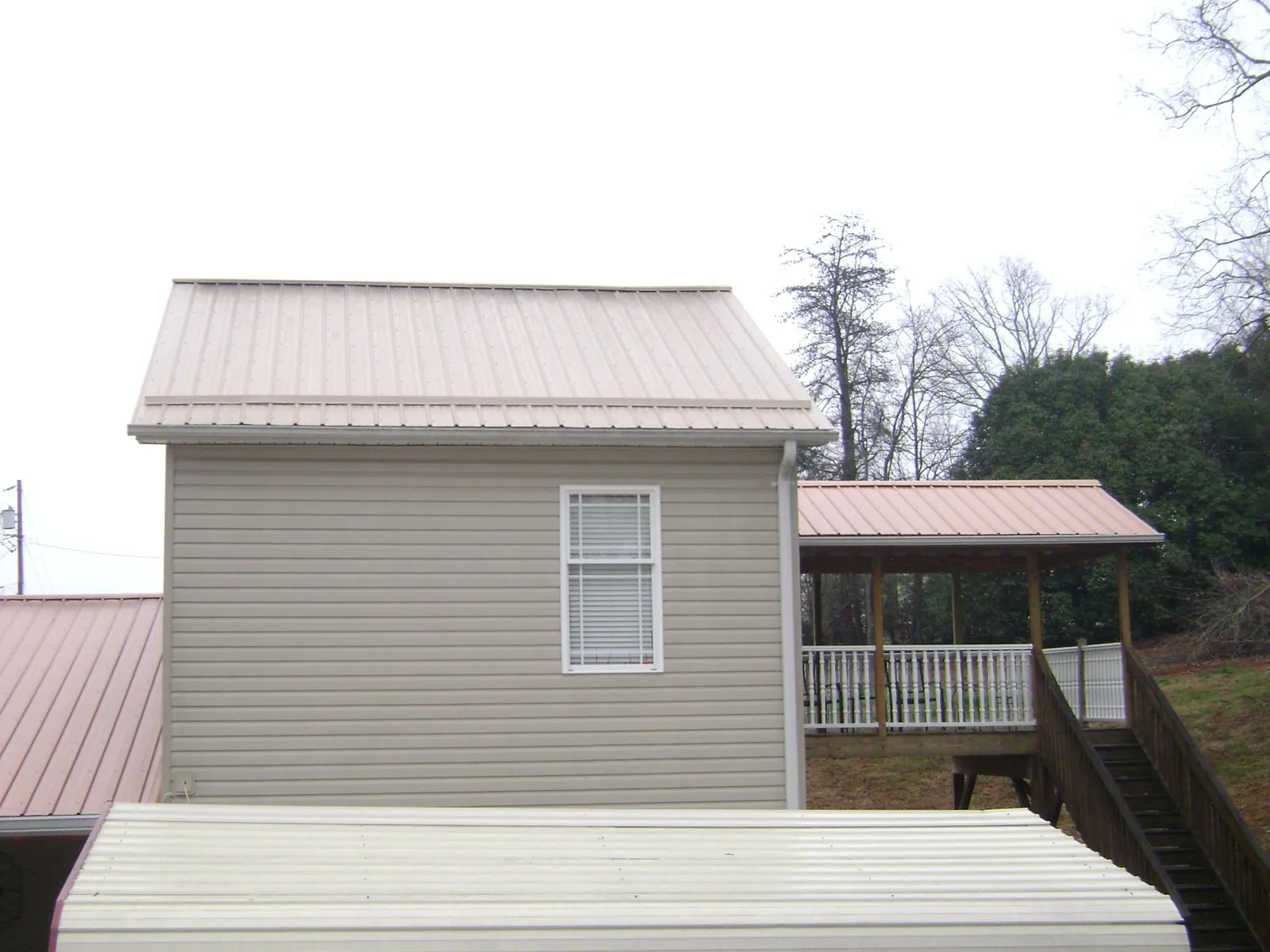 Tan metal roofs on a two story addition and attached porch, from a Roof Replacement job in Dighton